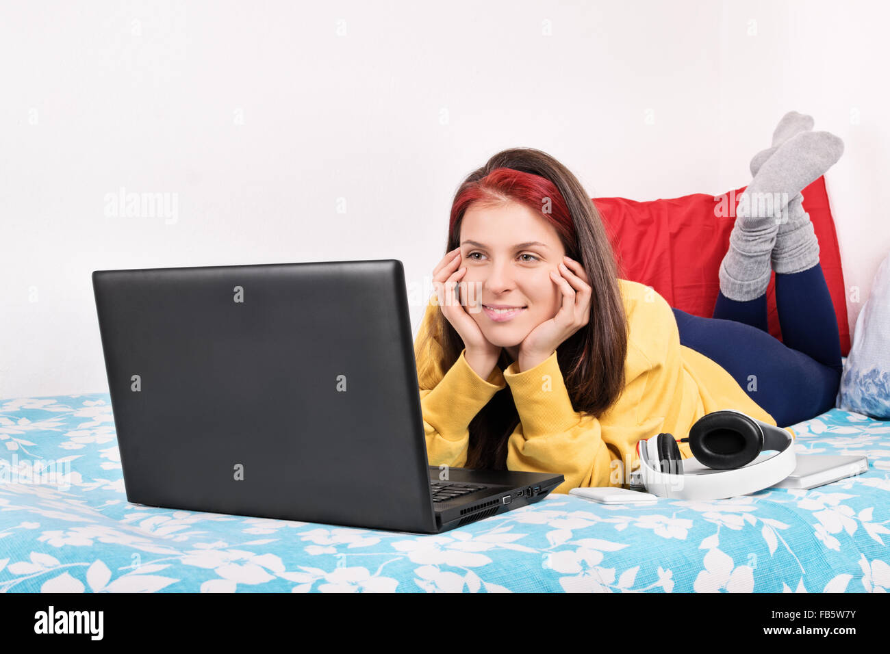 Belle jeune femme dans des vêtements confortables au lit regarder quelque chose sur son ordinateur portable et souriant. Banque D'Images