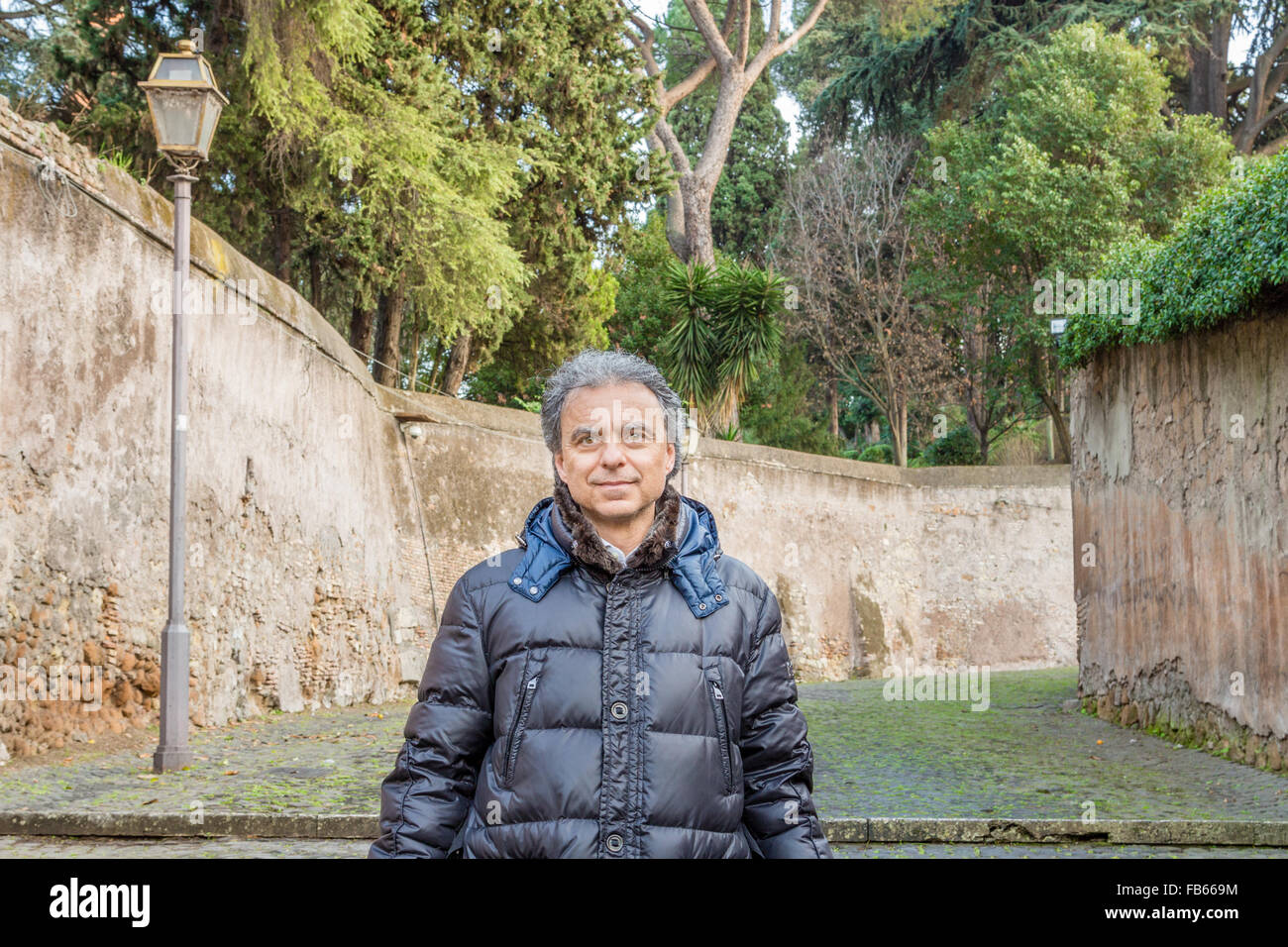 Homme de race blanche d'âge moyen aux cheveux gris vêtus de noir Down jacket debout dans une rue de l'ancienne Rome. Banque D'Images