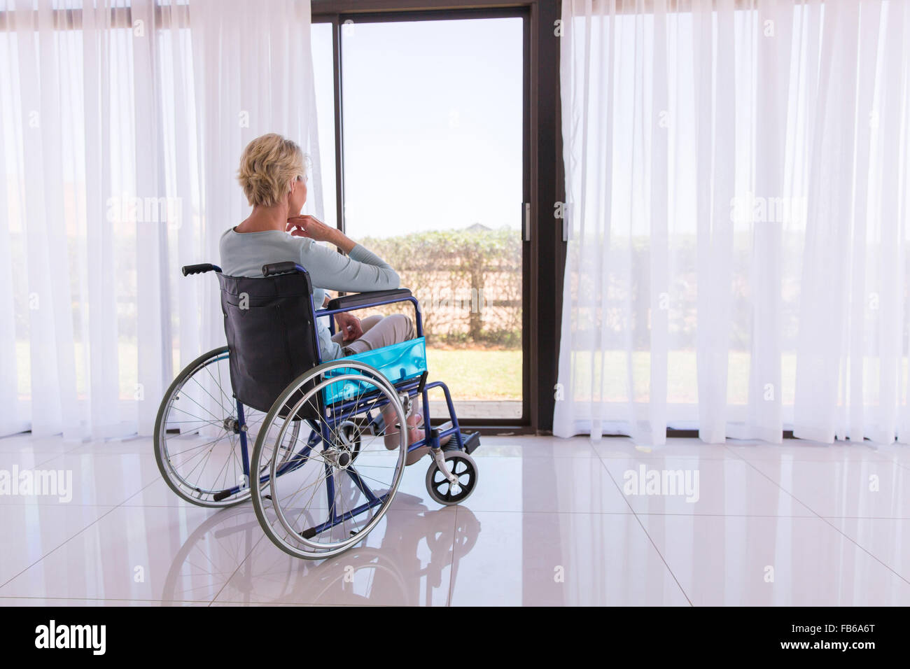 Mobilité réfléchie woman in wheelchair regardant à travers la vitre de la porte Banque D'Images