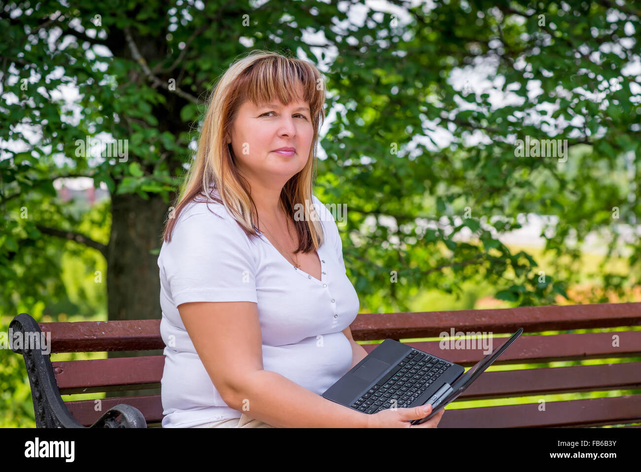 Belle femme mature sur un banc de parc avec un ordinateur portable Banque D'Images