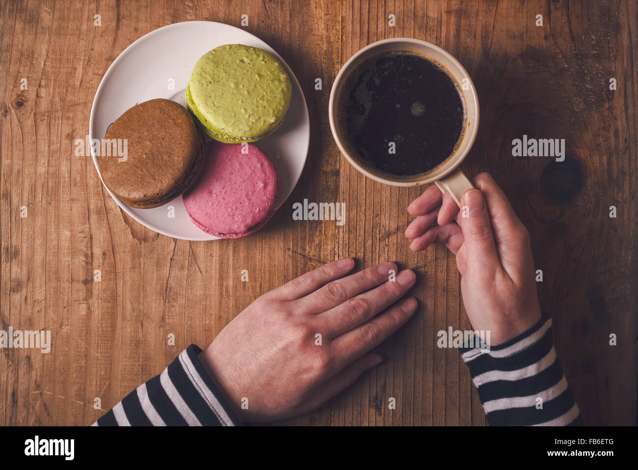 Café et biscuits macaron sur la table le matin, femme hand holding cup avec boisson chaude, vue d'en haut, aux couleurs rétro Banque D'Images