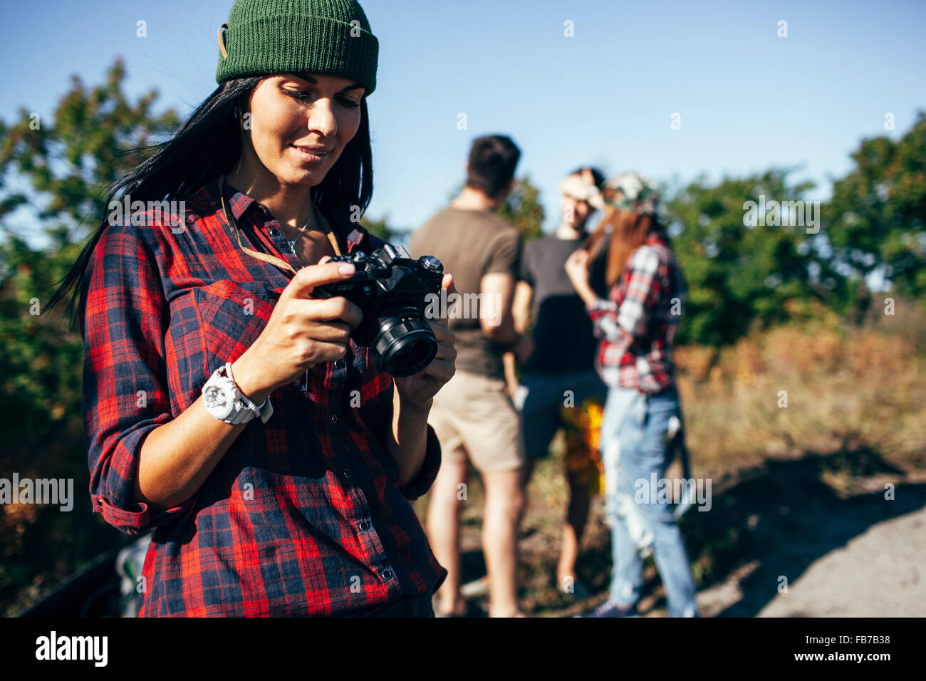 Jeune femme à la recherche de photographies sur l'appareil photo avec les amis standing in forest Banque D'Images