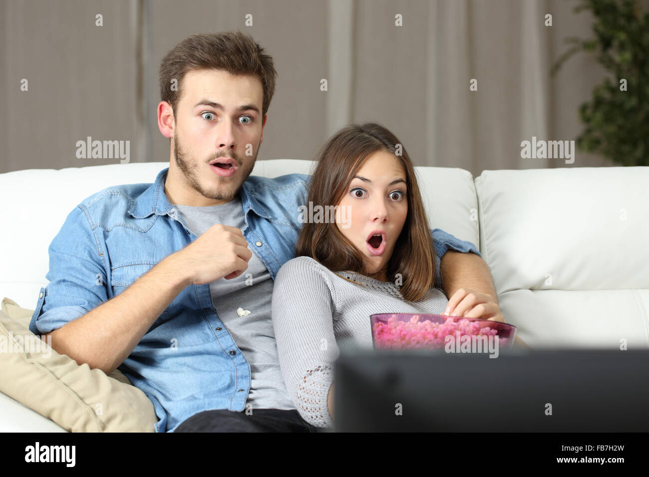 Surpris couple watching tv assis sur un canapé à la maison Banque D'Images