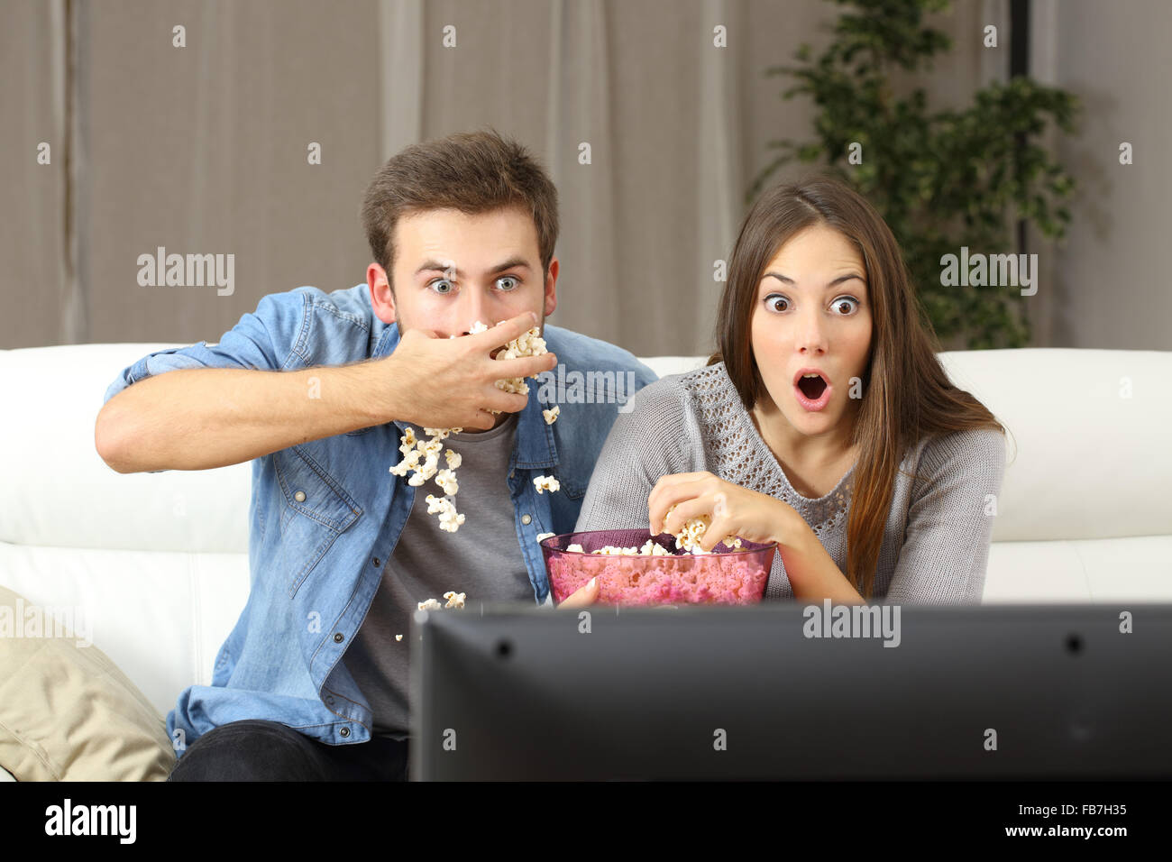 Surpris couple watching tv program assise sur un sofa à la maison Banque D'Images