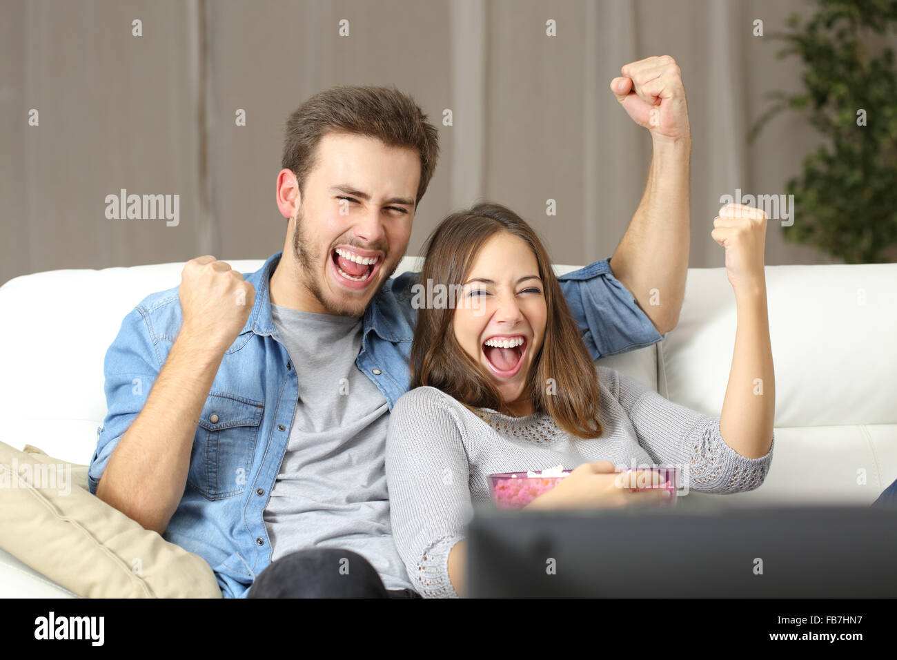 Couple euphorique de regarder la télévision assis sur un canapé à la maison Banque D'Images