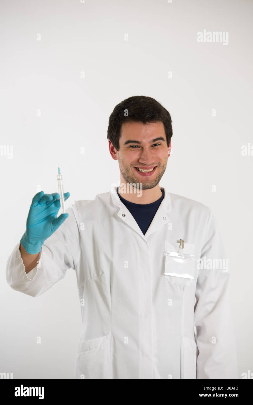 Jeune homme médecin, sur fond blanc, vêtu de blanc et bleu gants, détient seringue Banque D'Images
