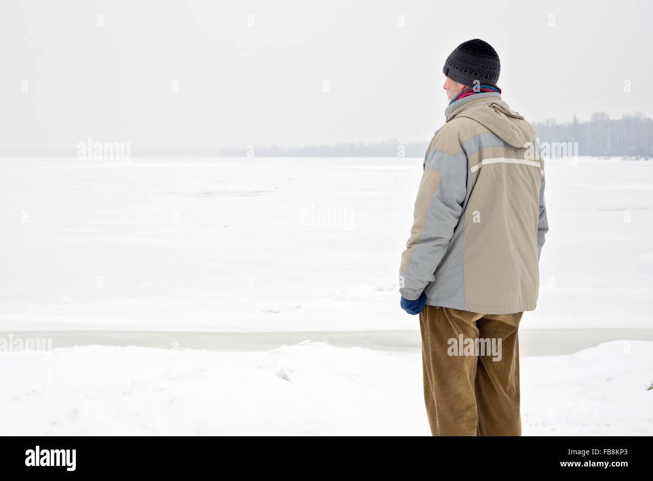 Un homme avec un chapeau en laine, une veste imperméable et un chapeau de laine est à la recherche à la rivière Dniepr lors d'une froide et triste hiver gris morn Banque D'Images