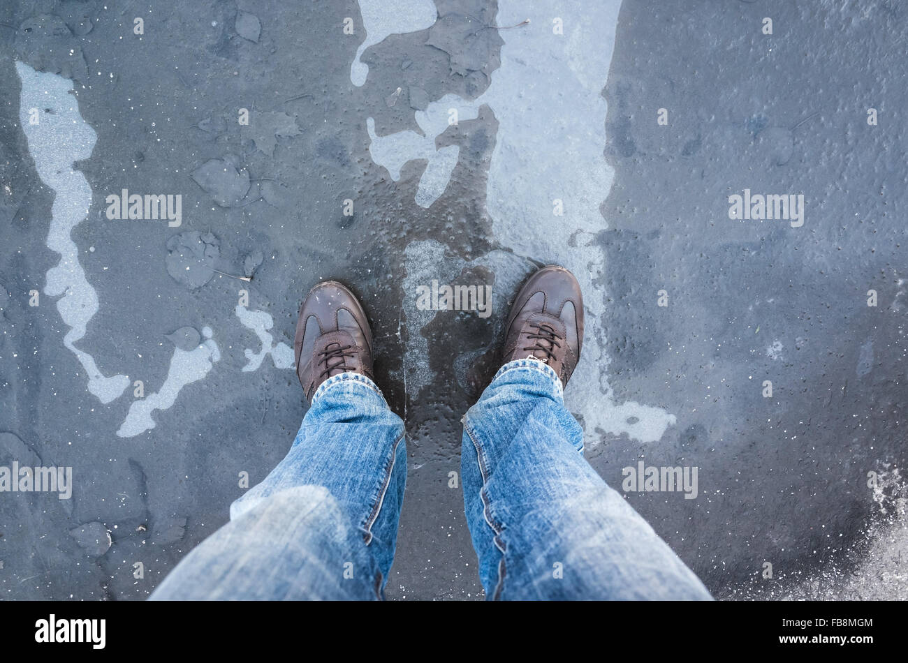 Homme debout sur pieds avec une fine couche de glace gelé flaque et les feuilles qui tombent Banque D'Images