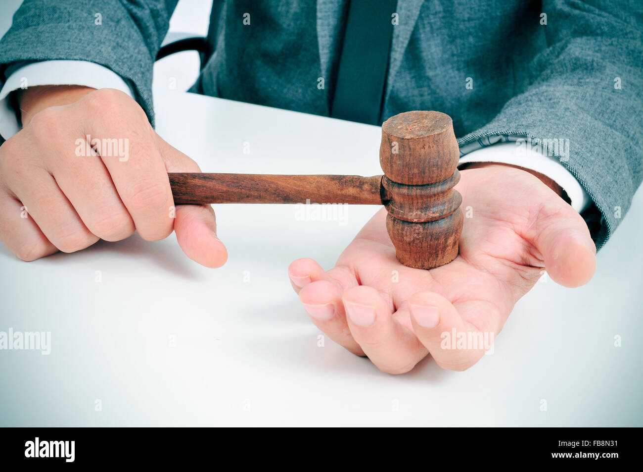 Closeup of a young man in suit assis dans un bureau avec un marteau en bois dans sa main Banque D'Images