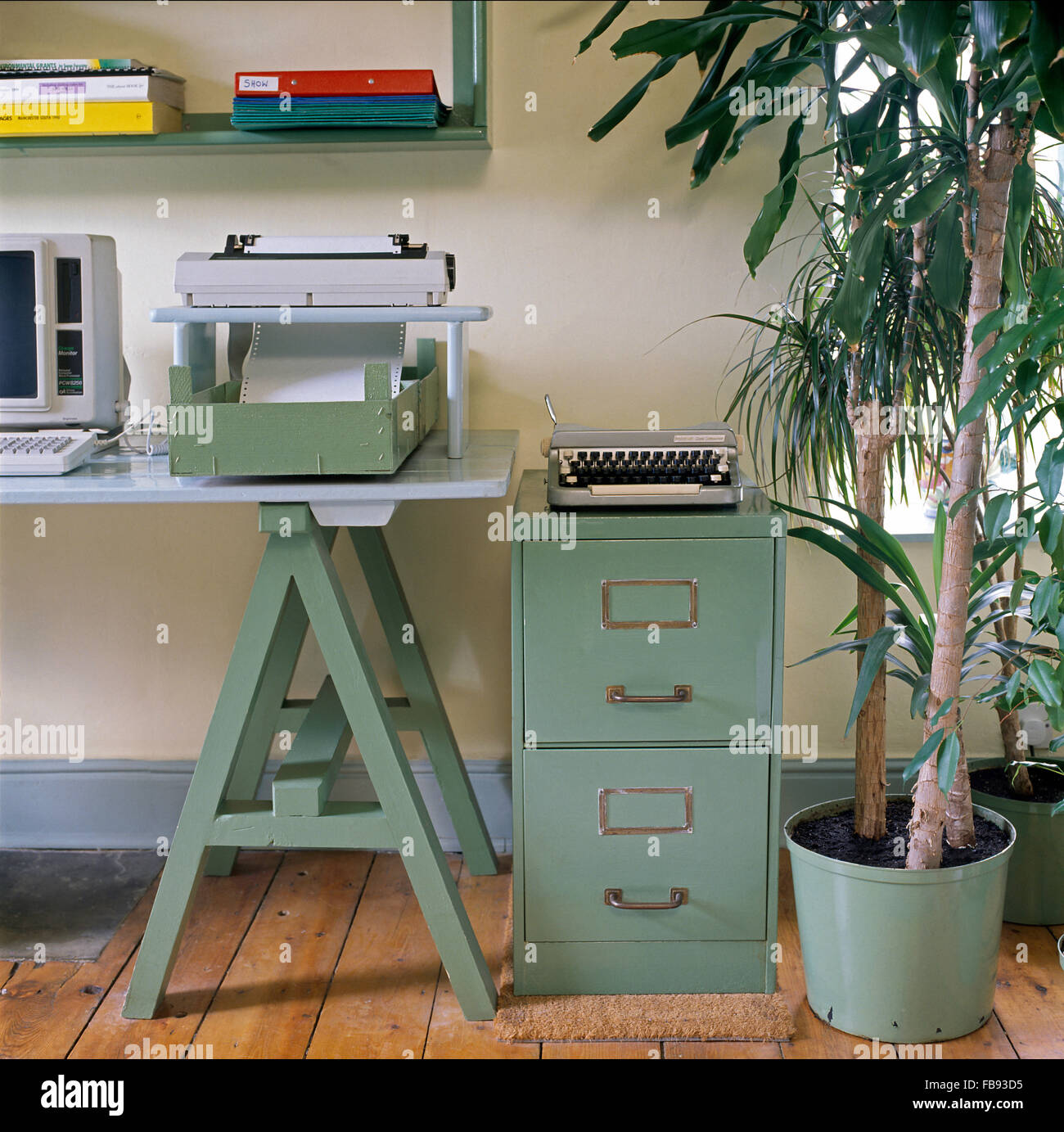 Imprimante sur table tréteau dans années 90 avec une machine à écrire vintage portable sur un meuble d'archivage et d'un turquoise grande plante Banque D'Images