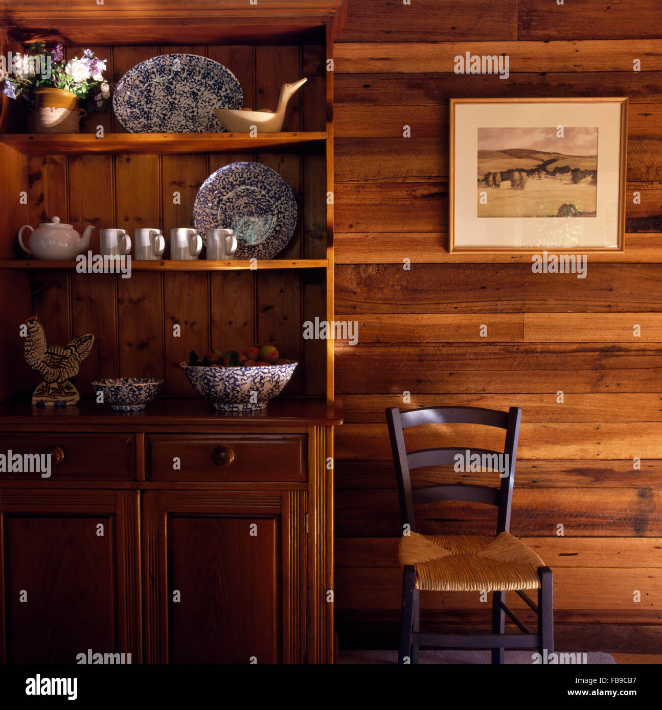 Commode en pin clair et rush assis vintage chaise contre un mur lambrissé de bois Banque D'Images