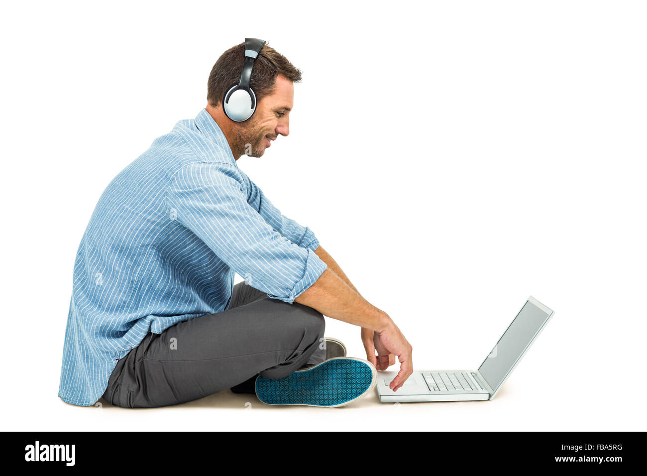 Smiling man sitting on floor using laptop et écouteurs Banque D'Images