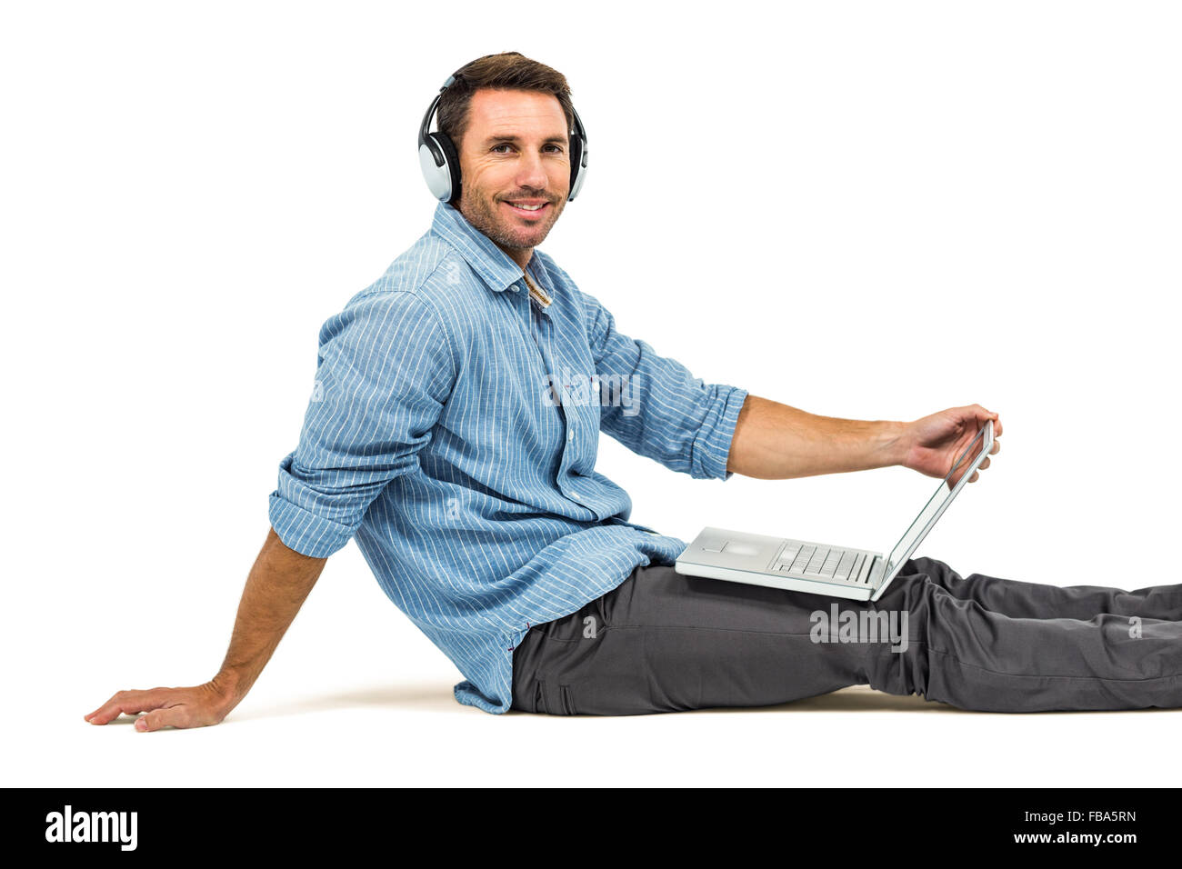 Happy man sitting on floor using laptop et écouteurs Banque D'Images