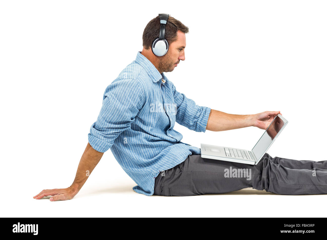 Homme assis sur le plancher à l'aide d'ordinateur portable et un casque Banque D'Images
