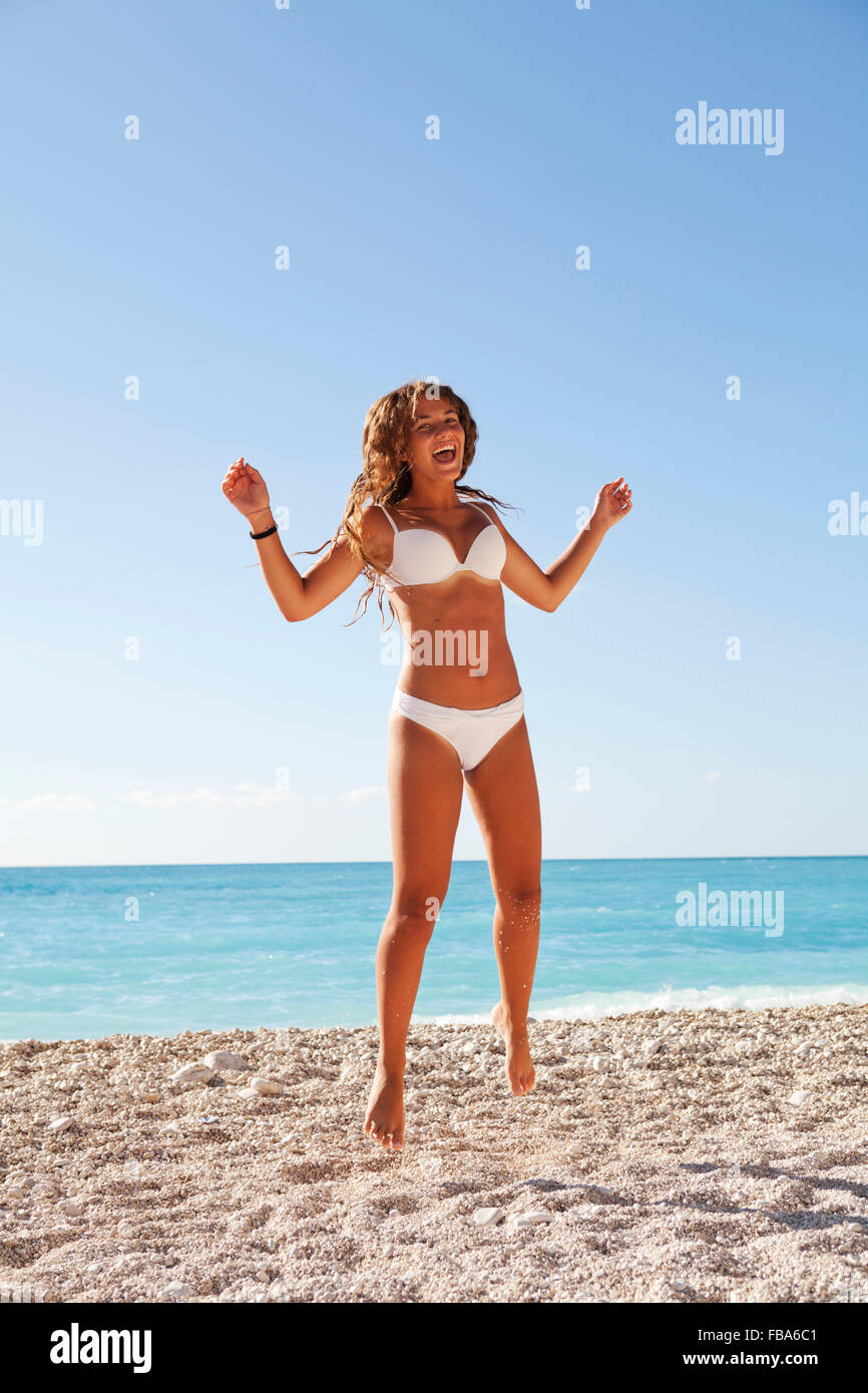 Beautiful young girl wearing bikini blanc sautant dans les couleurs bleu de Plage de Myrtos, Kefalonia, Grèce Banque D'Images