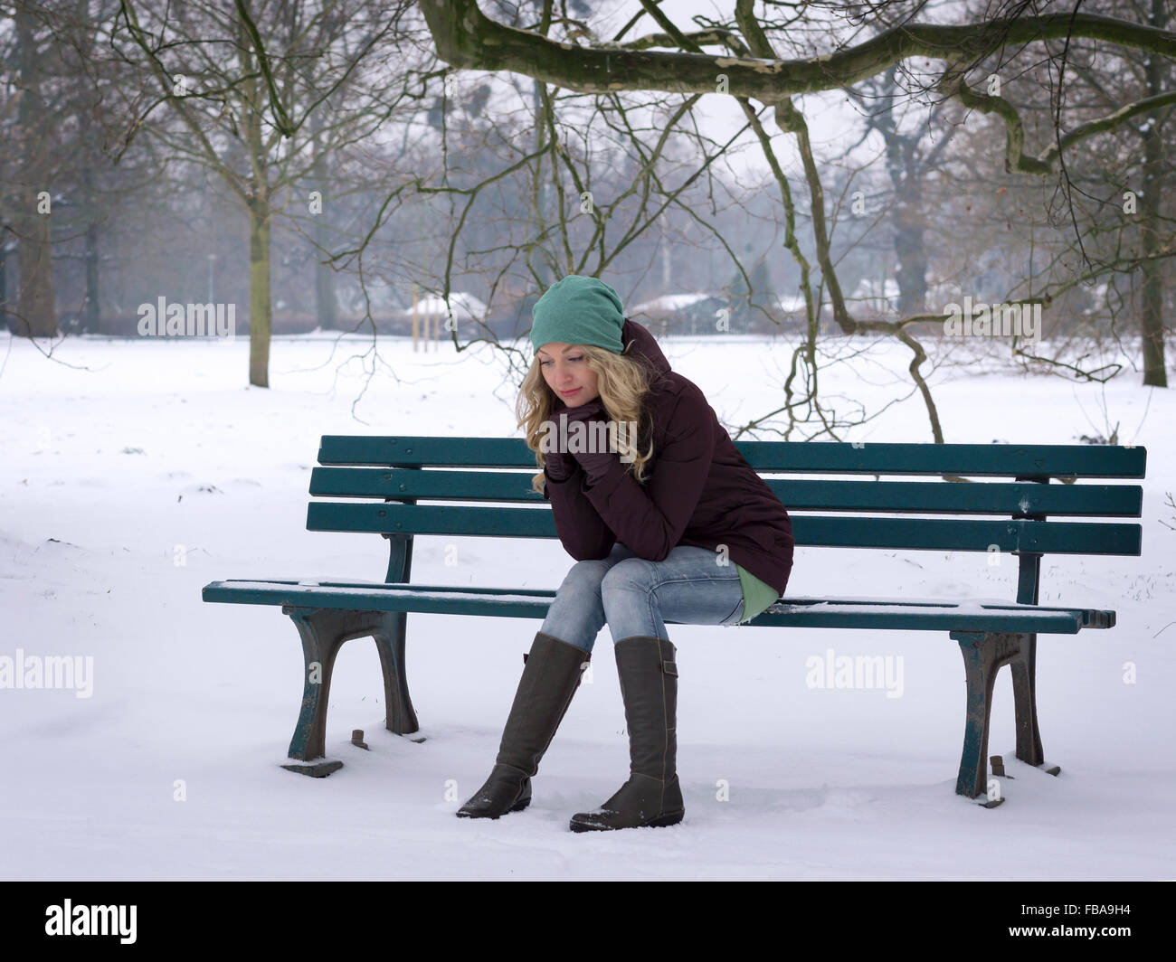 Femme assise seule sur le banc de parc en hiver Banque D'Images