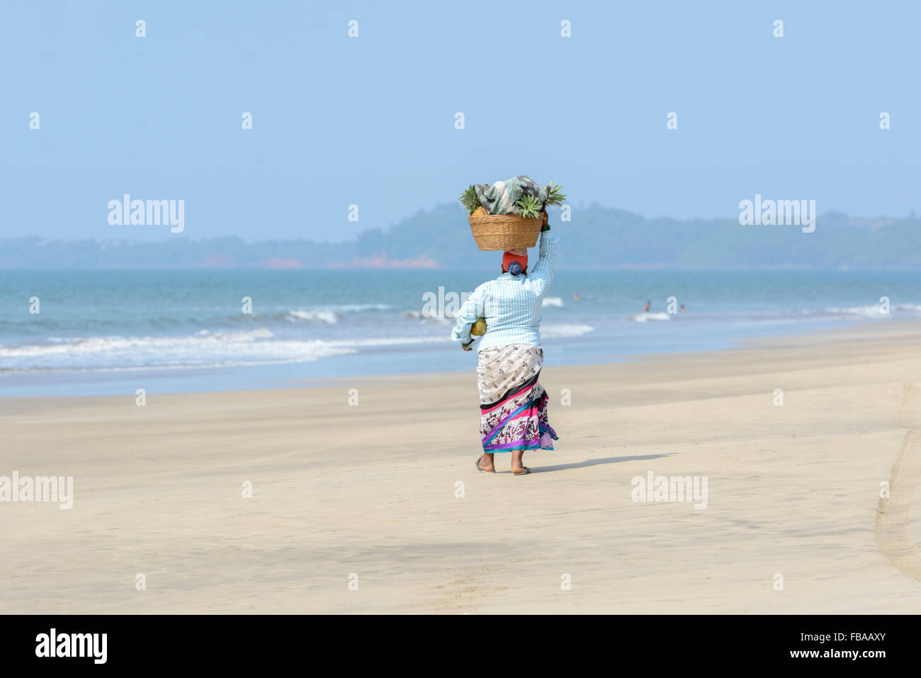 Une femme indienne vendant des fruits et des boissons promenades le long d'une plage vide, plage de Mandrem, Nord de Goa, Inde Banque D'Images