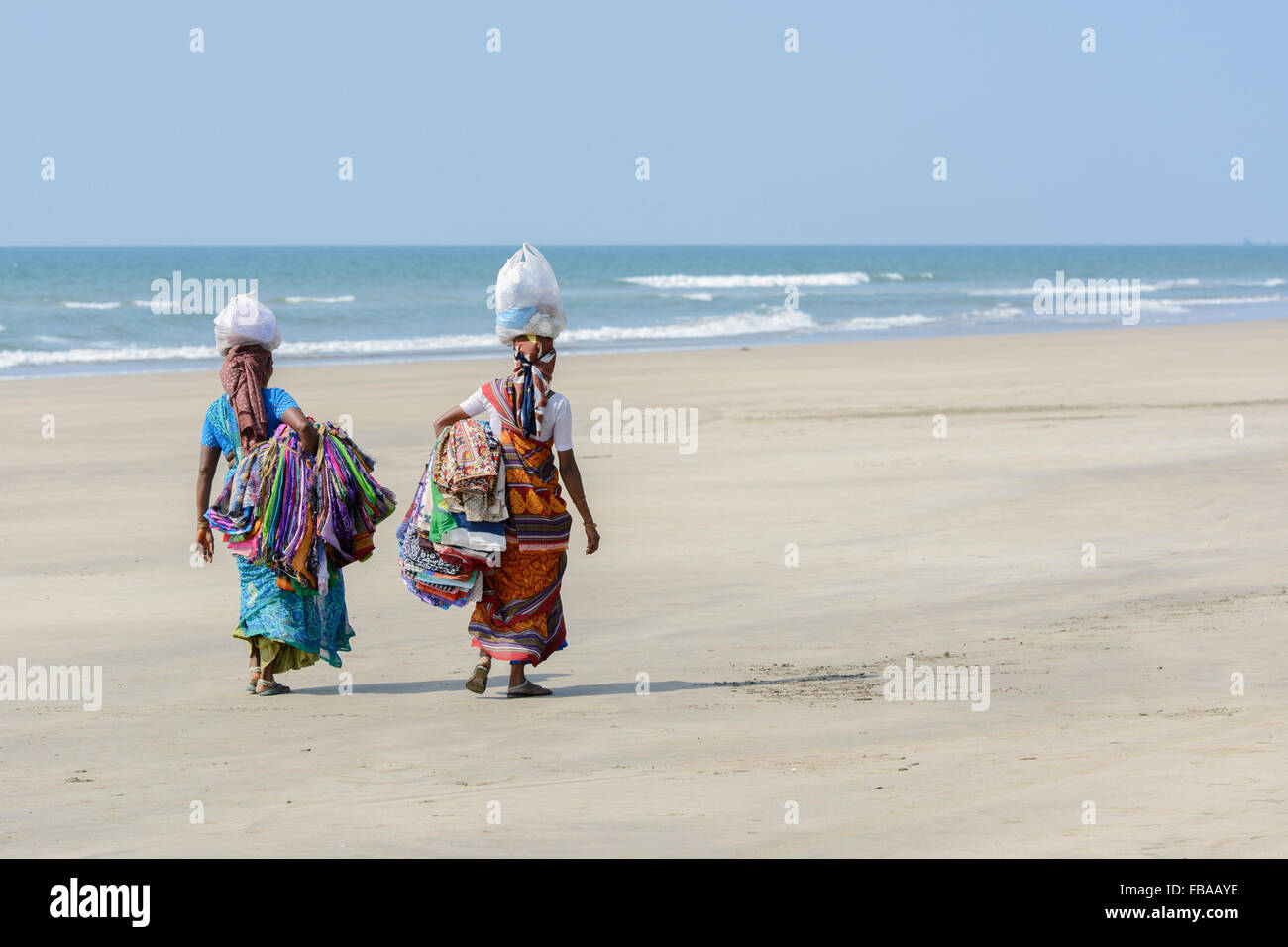 Deux femmes indiennes vendant des sarongs et tissus marche sur une plage vide, plage de Mandrem, Nord de Goa, Inde Banque D'Images