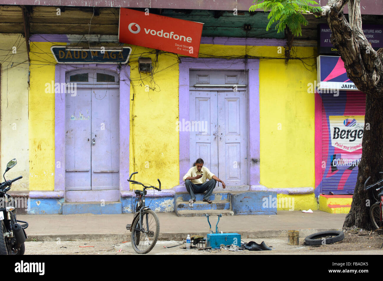 Indian man sitting on steps reading messages téléphone mobile vodafone sous un signe à Panaji (Panjim), Nord de Goa, Inde Banque D'Images