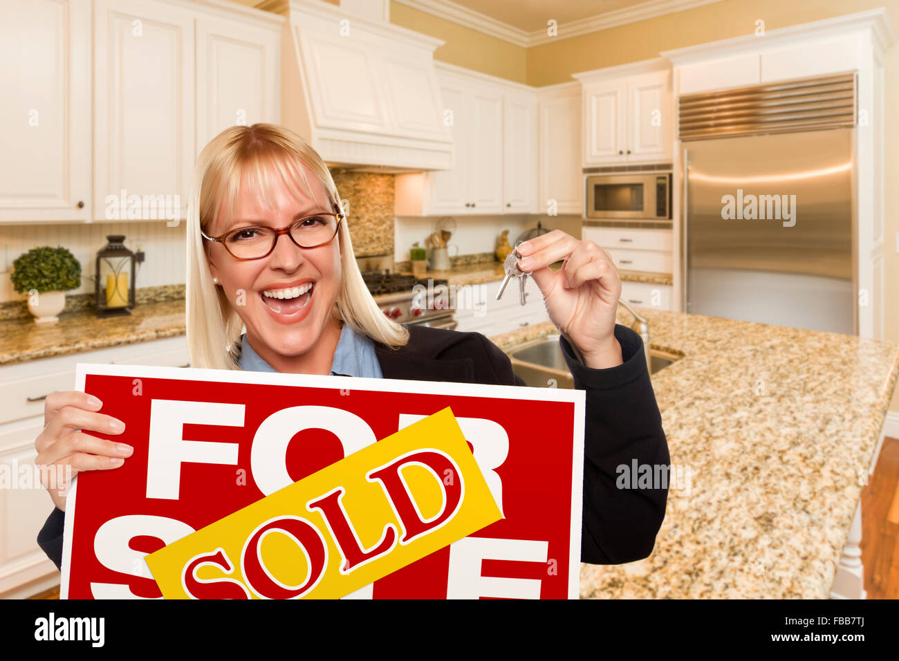 Happy Young Woman Holding a vendu Achat Immobilier signe et clés à l'intérieur de belle cuisine sur mesure. Banque D'Images