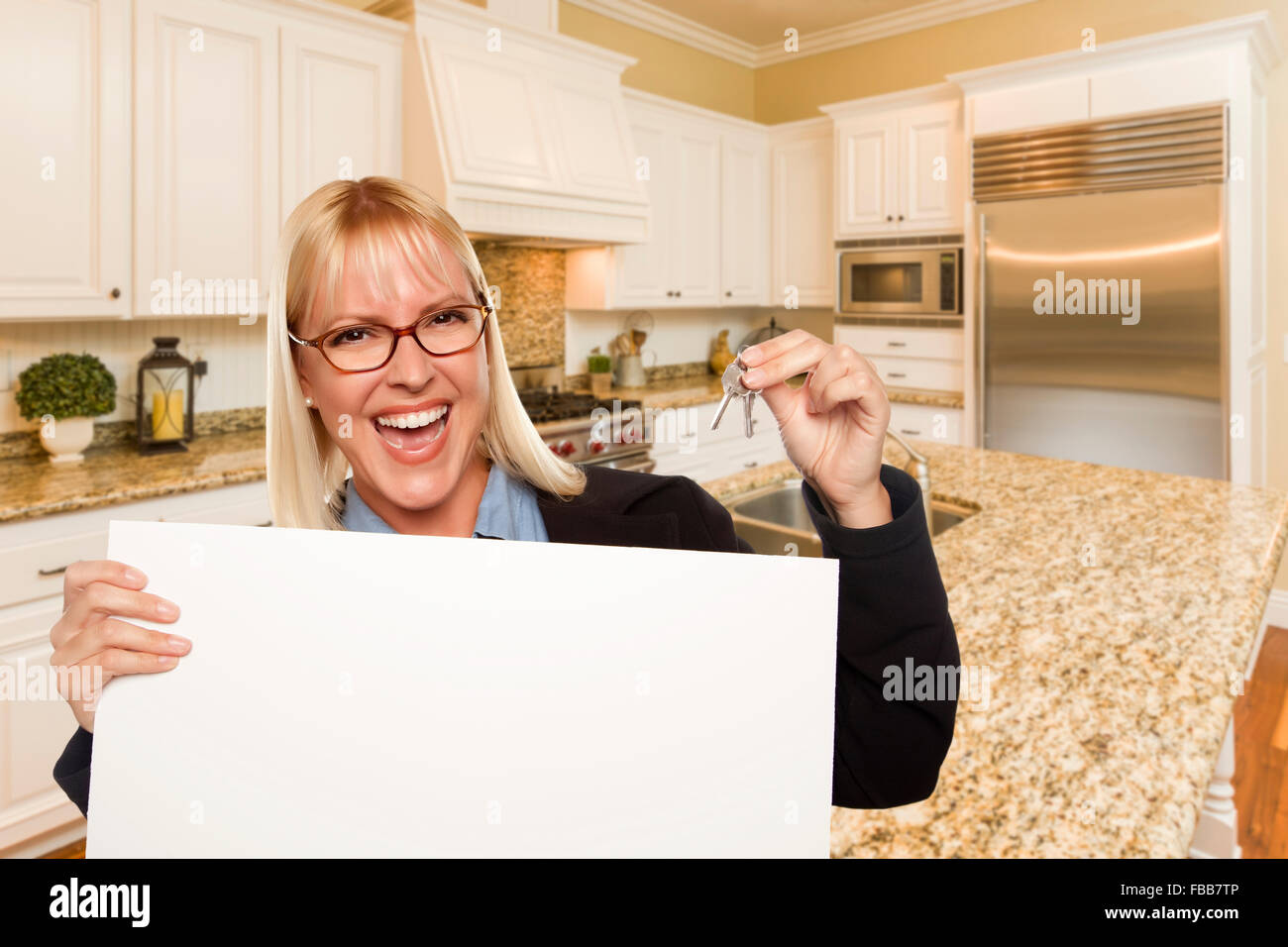 Happy Young Woman Holding Blank Sign et clés à l'intérieur de belle cuisine sur mesure. Banque D'Images