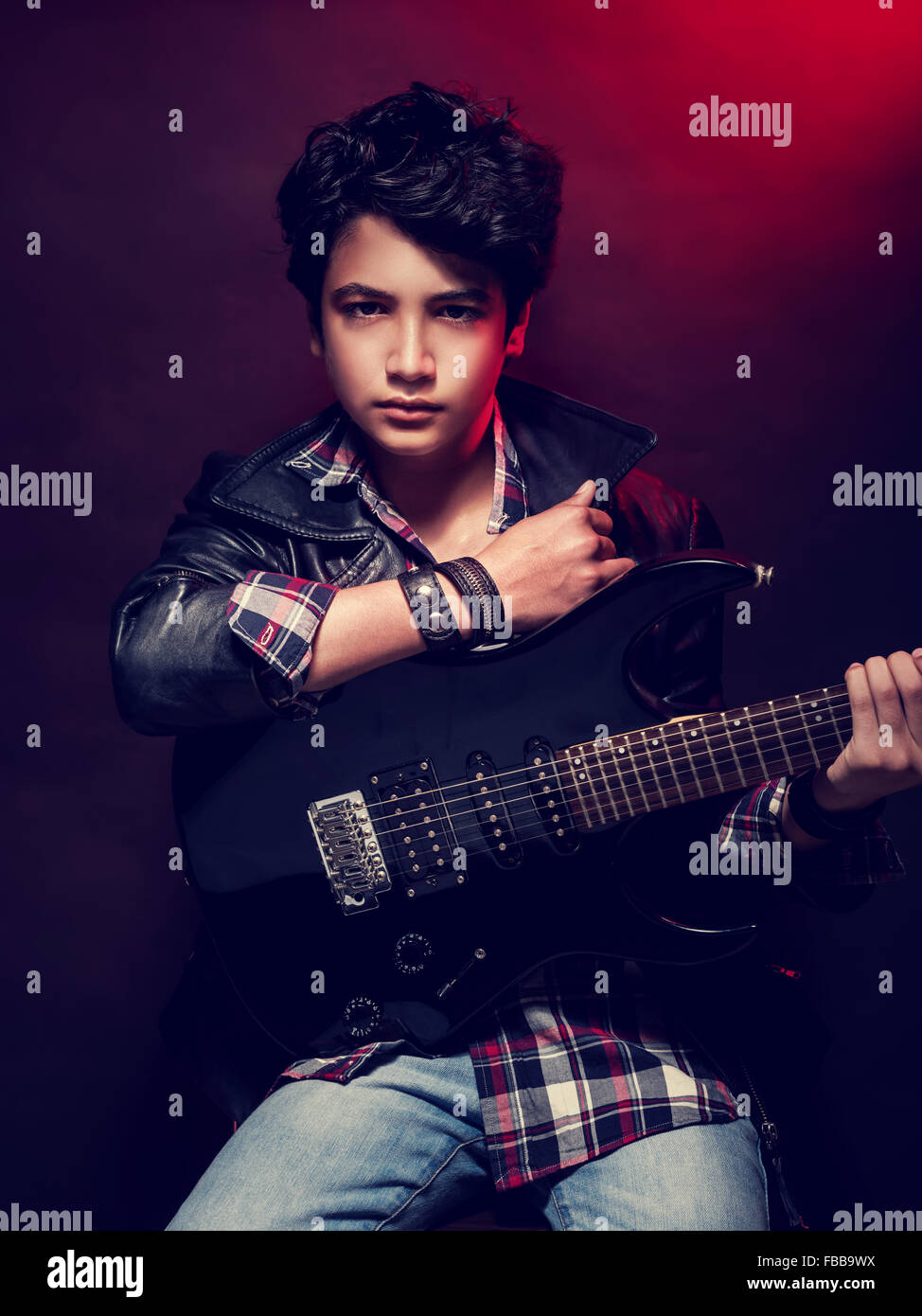 Sérieux talent teen boy avec guitare sur fond rouge sombre, jouant sur l'instrument de musique, de vie heureuse Banque D'Images