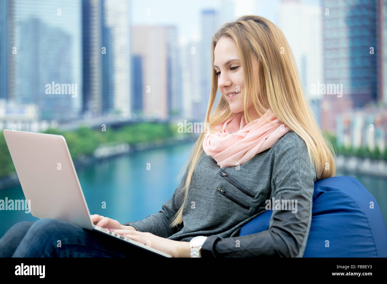 Jeune fille à l'aide d'ordinateur portable, d'étudier, de travailler, de communiquer, de commander en ligne, assis dans un confortable fauteuil poire, paysage urbain sur la Banque D'Images