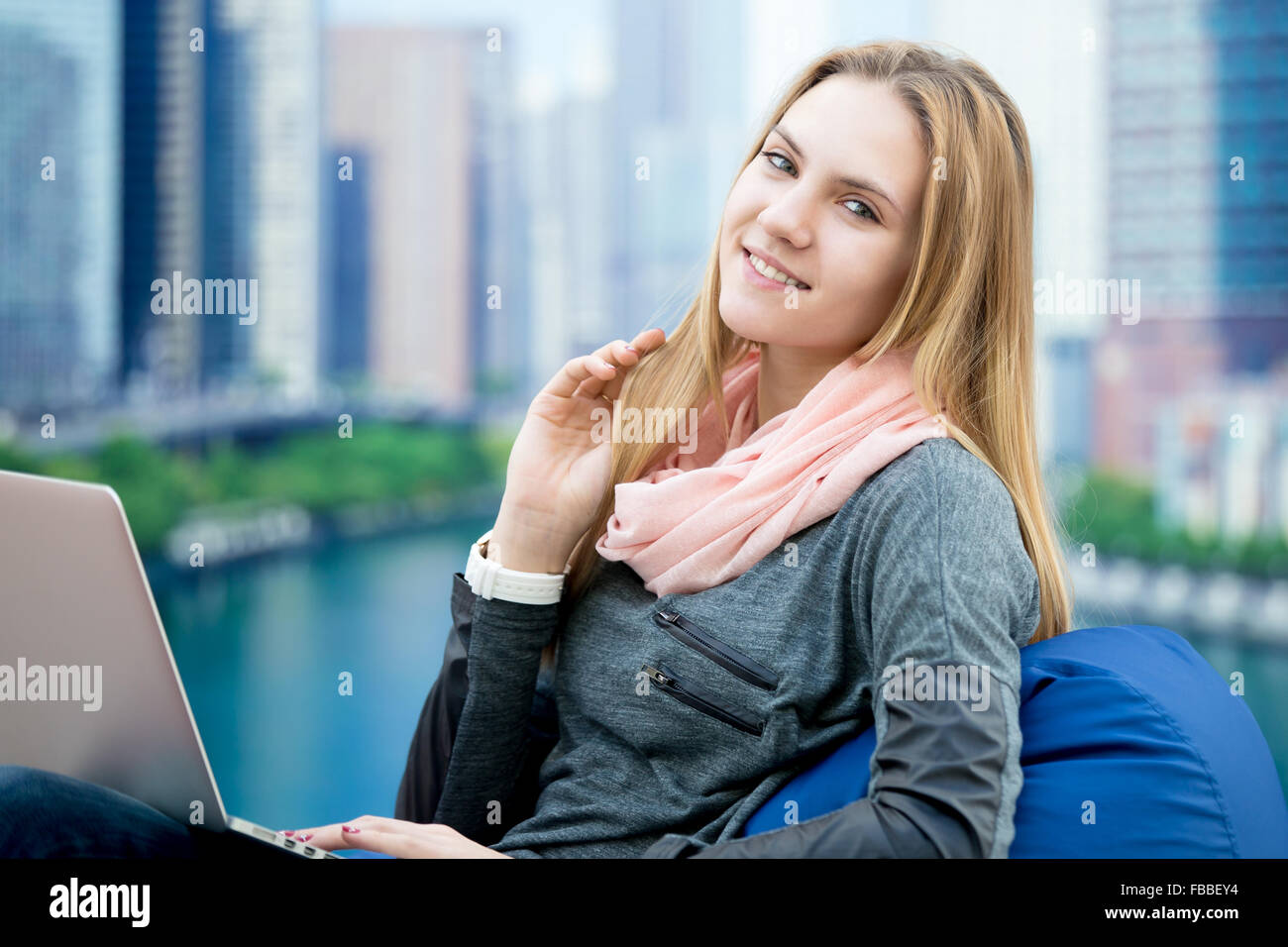 Happy smiling girl sitting dans de confortables chaise de sac d'haricot avec son ordinateur portable, grande ville sur l'arrière-plan Banque D'Images