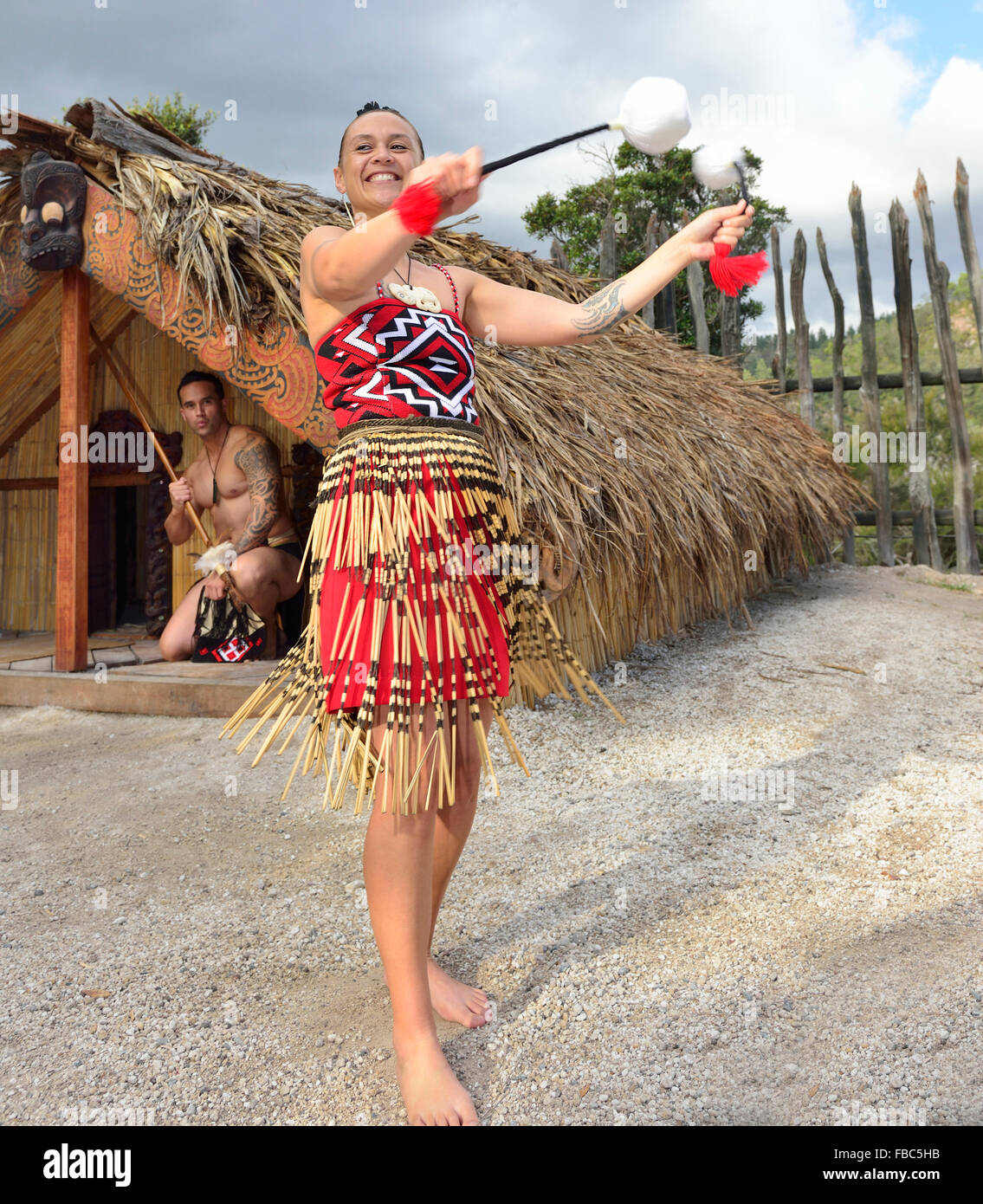 Femme maorie et homme maori à te Puia Maori Village Rotorua. La femme danse avec des POI(s) alors que l'homme est dans la cabane derrière. Île du Nord, Nouvelle-Zélande Banque D'Images