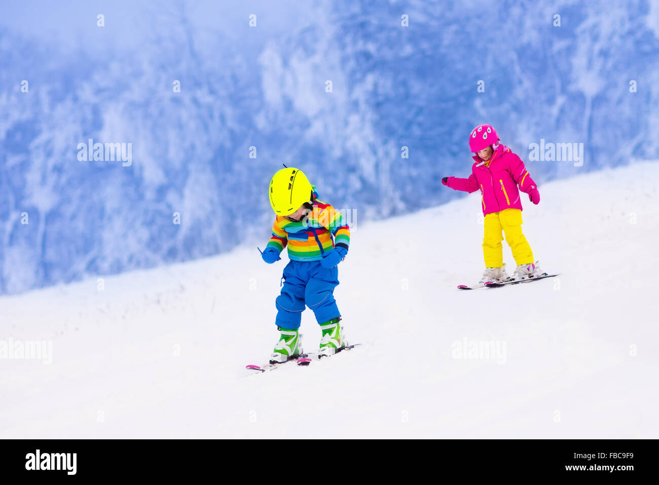 Les enfants de ski dans les montagnes. Tout-petits enfants en costume coloré et casque de sécurité l'apprentissage du ski. Sport d'hiver pour la famille Banque D'Images