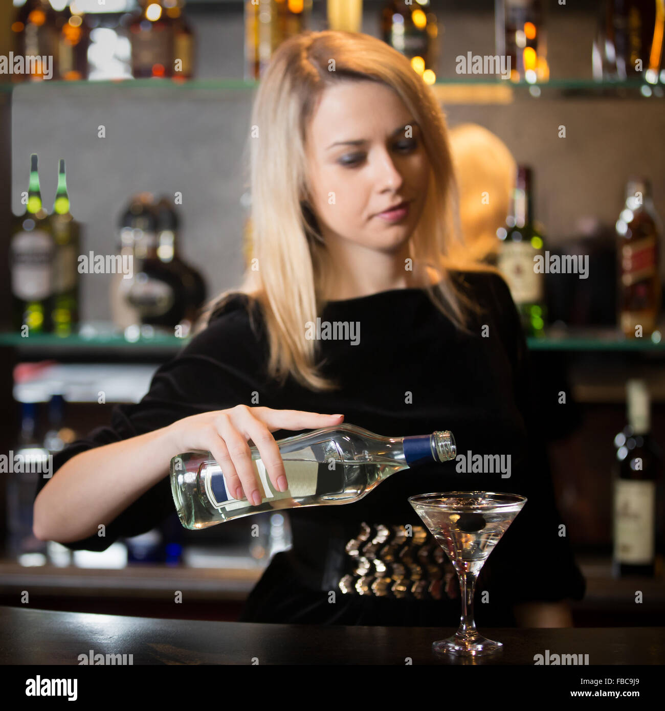 Belle blonde fille barman de servir de l'alcool boire au comptoir du bar, le coulage de verre en verre à cocktail, se concentrer sur la bouteille dans la main Banque D'Images