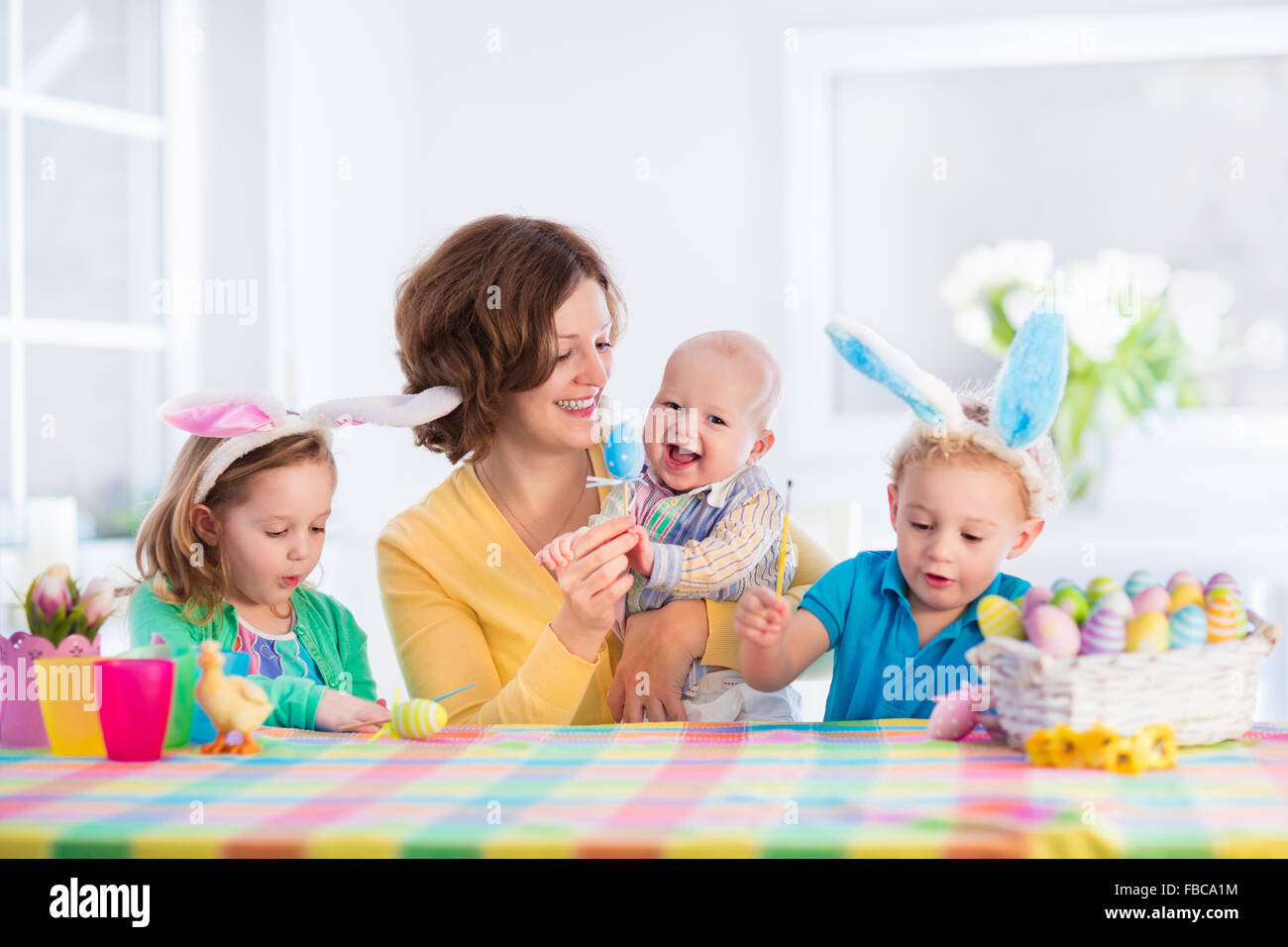 Mère et enfants oeufs colorés de peinture. Maman, bébé, enfant et bébé avec oreilles de lapin peindre et décorer des oeufs de Pâques. Banque D'Images