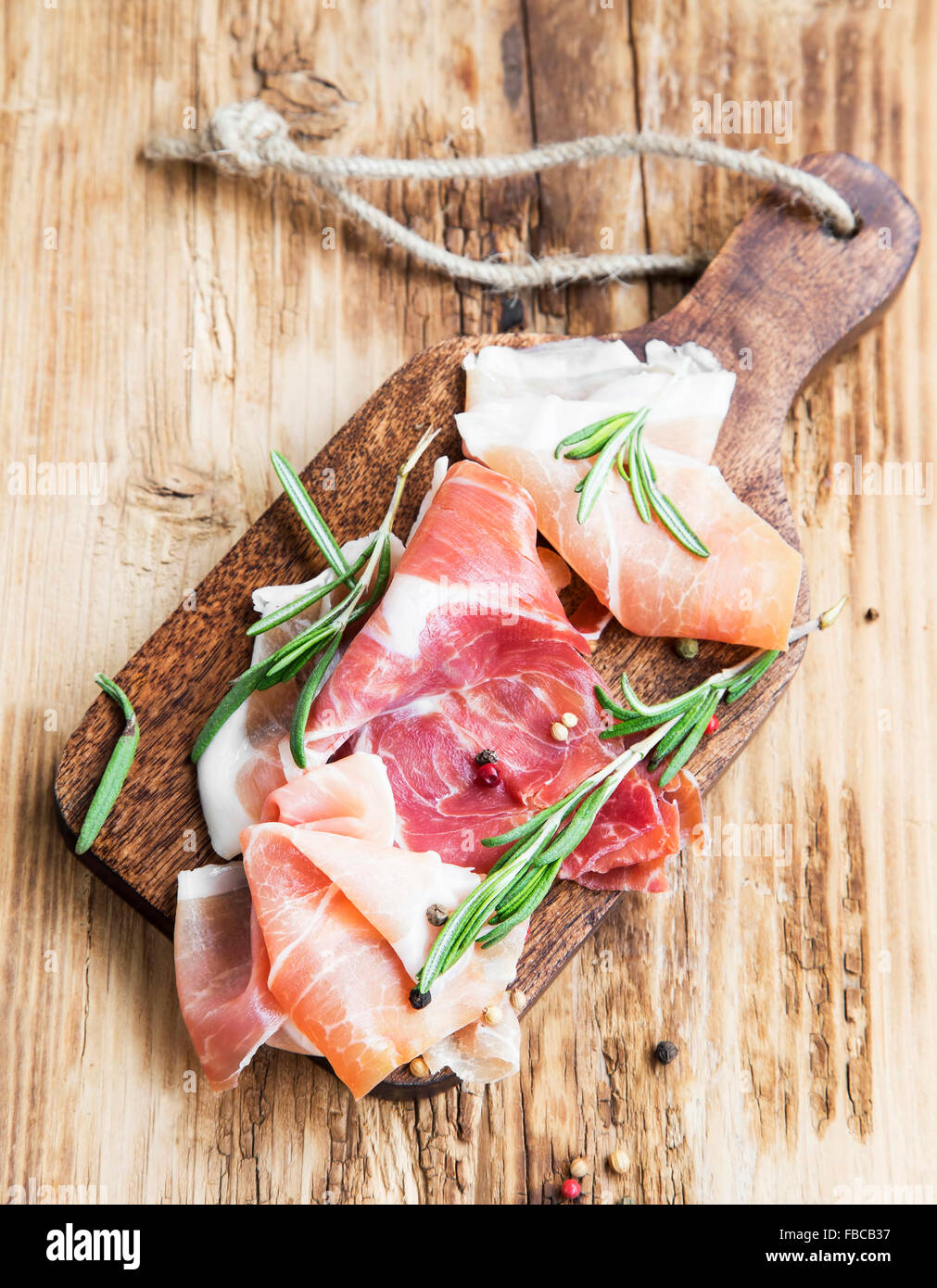 Jambon Jambon Serrano avec le romarin et le poivre piquant sur une planche à découper en bois Banque D'Images