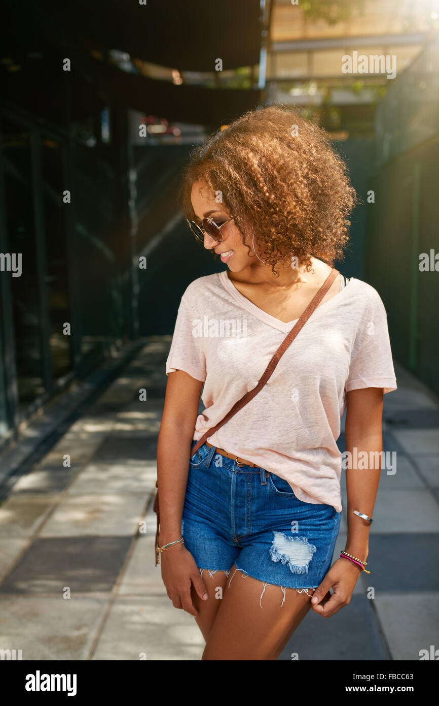 Young African American city girl. Elle porte tenue décontractée, lunettes de soleil et à la recherche vers le bas. Banque D'Images