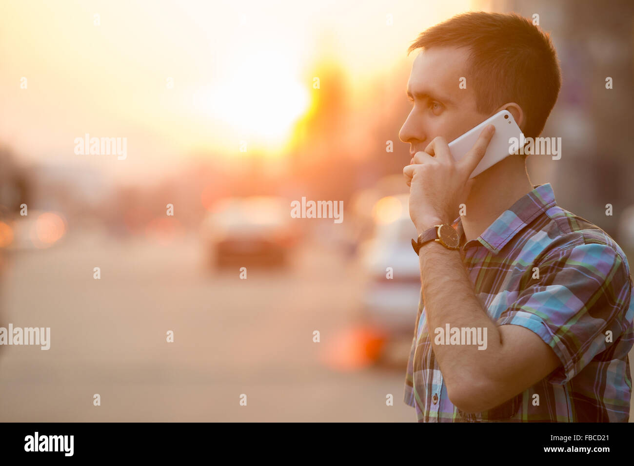 Young man holding mobile phone, smartphone, à l'aide d'un appel, parler au téléphone, debout sur la rue ensoleillée avec transports t Banque D'Images