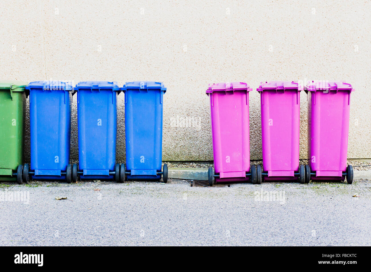 Une rangée de poubelles en plastique pour la collecte en face d'un mur de pierre Banque D'Images