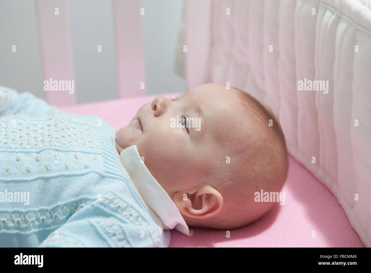 Quatre mois éveil bébé garçon couché dans lit bébé avec tampon amortisseur. Vue de côté Banque D'Images