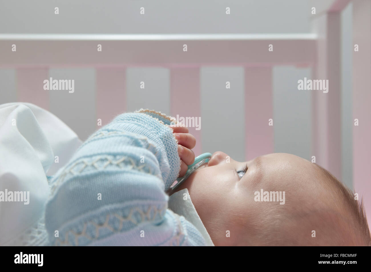 Quatre mois éveil bébé garçon couché dans lit bébé avec tétine. Vue de côté Banque D'Images