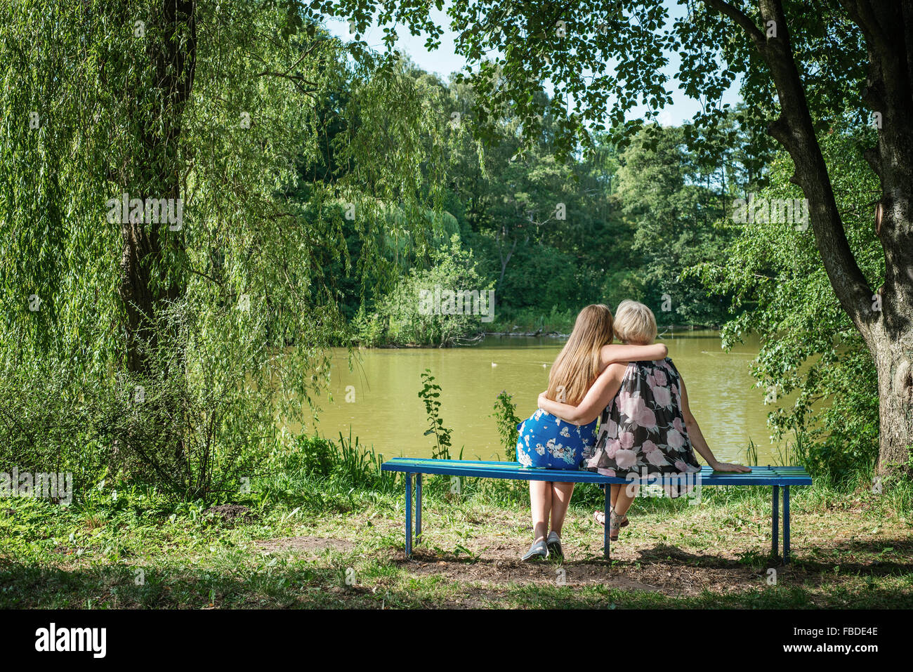 Deux femmes de générations différentes assis sur un banc près d'un étang en été. Mother and Daughter hugging. Banque D'Images
