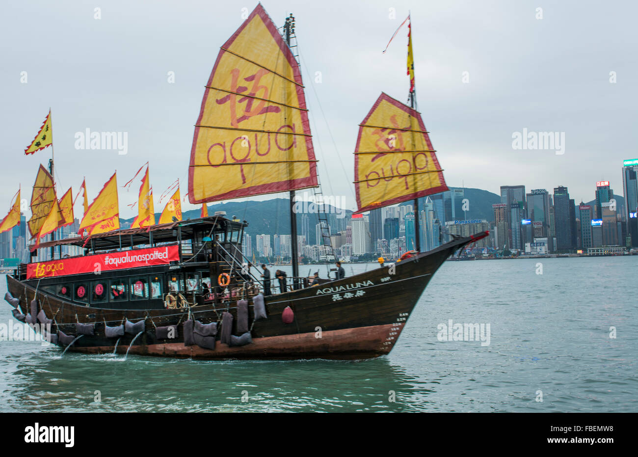 Chine Hong Kong skyline à partir de l'eau avec jonque traditionnelle jaune avec les ISC de la publicité contre l'arrière-plan de la ville Banque D'Images