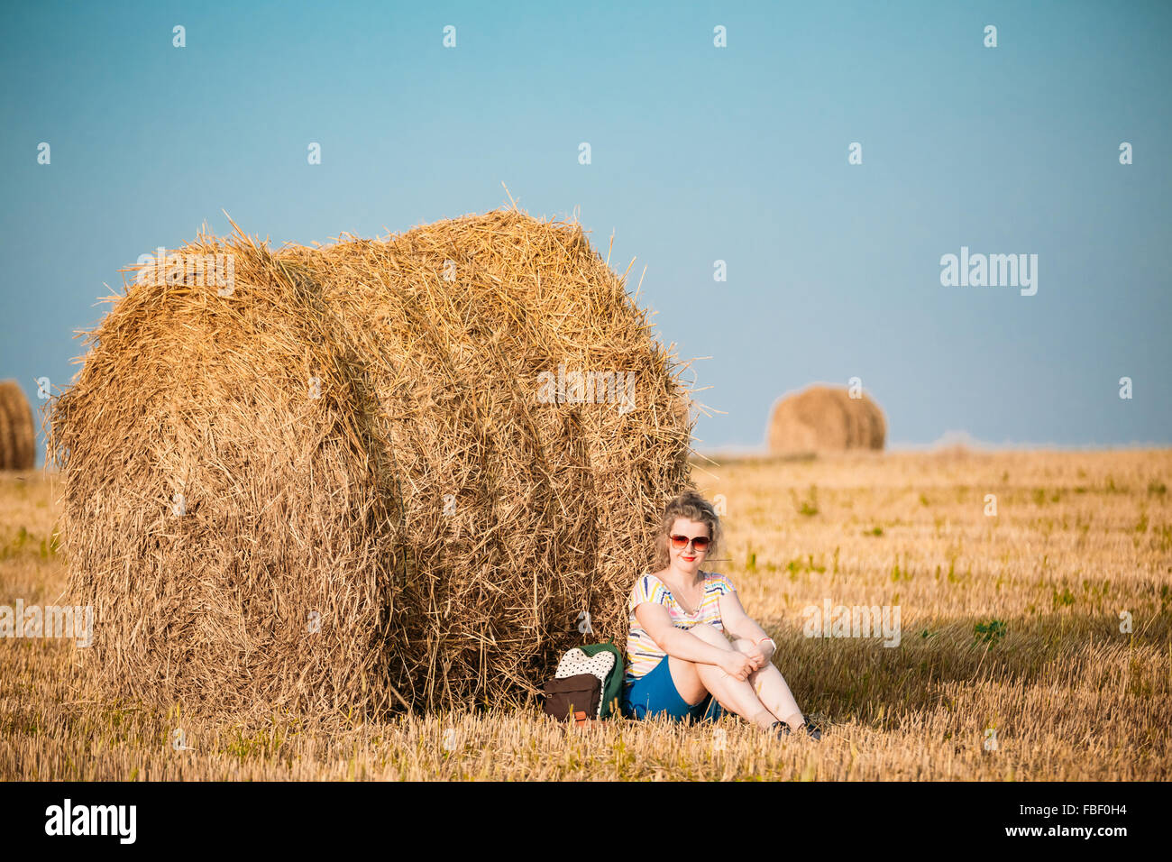 Taille Plus belle jeune femme de Shirt posant en été pré Champ des balles de foin au fond Coucher de soleil Banque D'Images