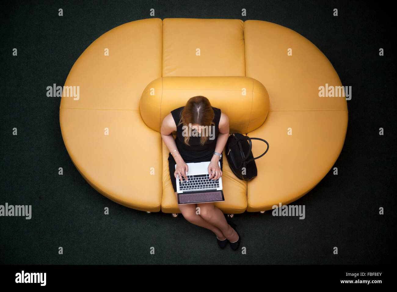Jeune femme assise sur yellow coach working on laptop in public zone wifi, dactylographie, vue du dessus Banque D'Images