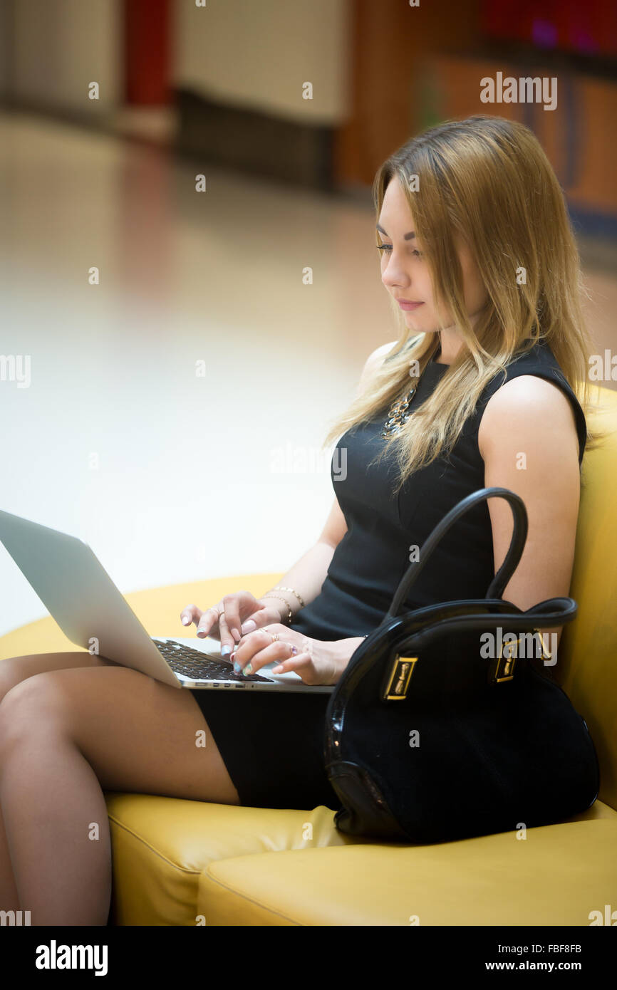 Belle Jeune femme assise sur yellow coach working on laptop in public zone wifi, dactylographie Banque D'Images