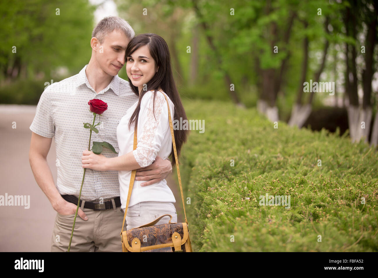 Young smiling woman holding Red Rose, looking at camera in park, son petit ami l'étreindre avec expression passionnée, copie savs Banque D'Images