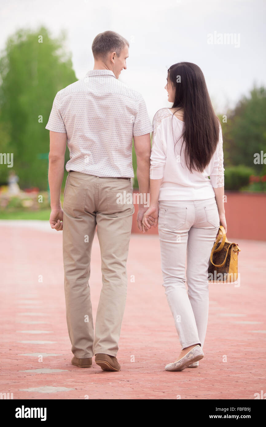 Couple d'amants, séduisant jeune homme et femme recherchant, marcher main dans la main dans la région de park, pleine longueur, vue arrière Banque D'Images