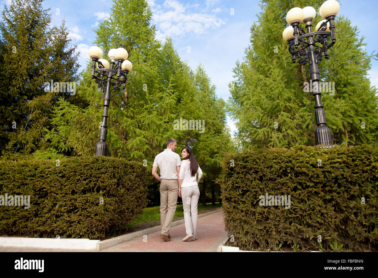 Couple d'amants, séduisant jeune homme et femme sur la date, la marche dans le parc avec des buissons taillés, tenant les mains, smiling girlfriend Banque D'Images