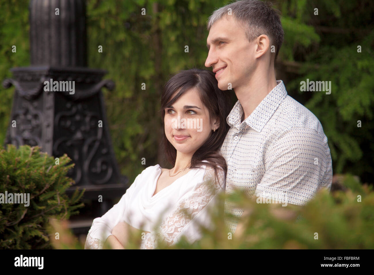 Couple d'amoureux assis sur un banc de parc sur une date, de détente en plein air avec des expressions de rêve, jeune homme serrant ses être Banque D'Images