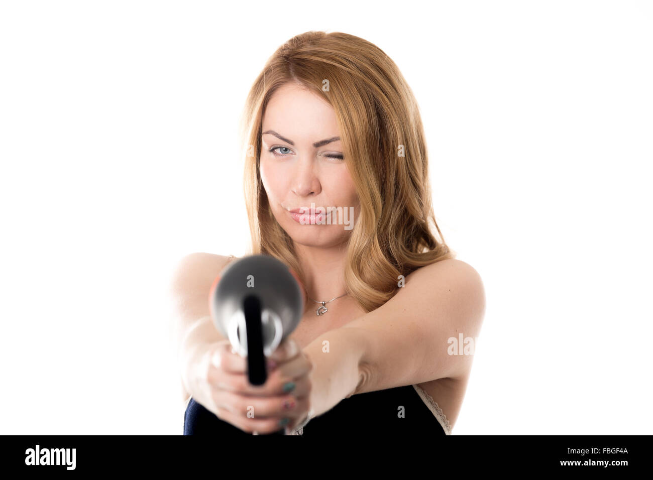 Les jeunes funny attractive blonde woman holding des sottises, sèche-cheveux noir comme l'arme dirigée vers l'appareil photo, l'accent sur Banque D'Images