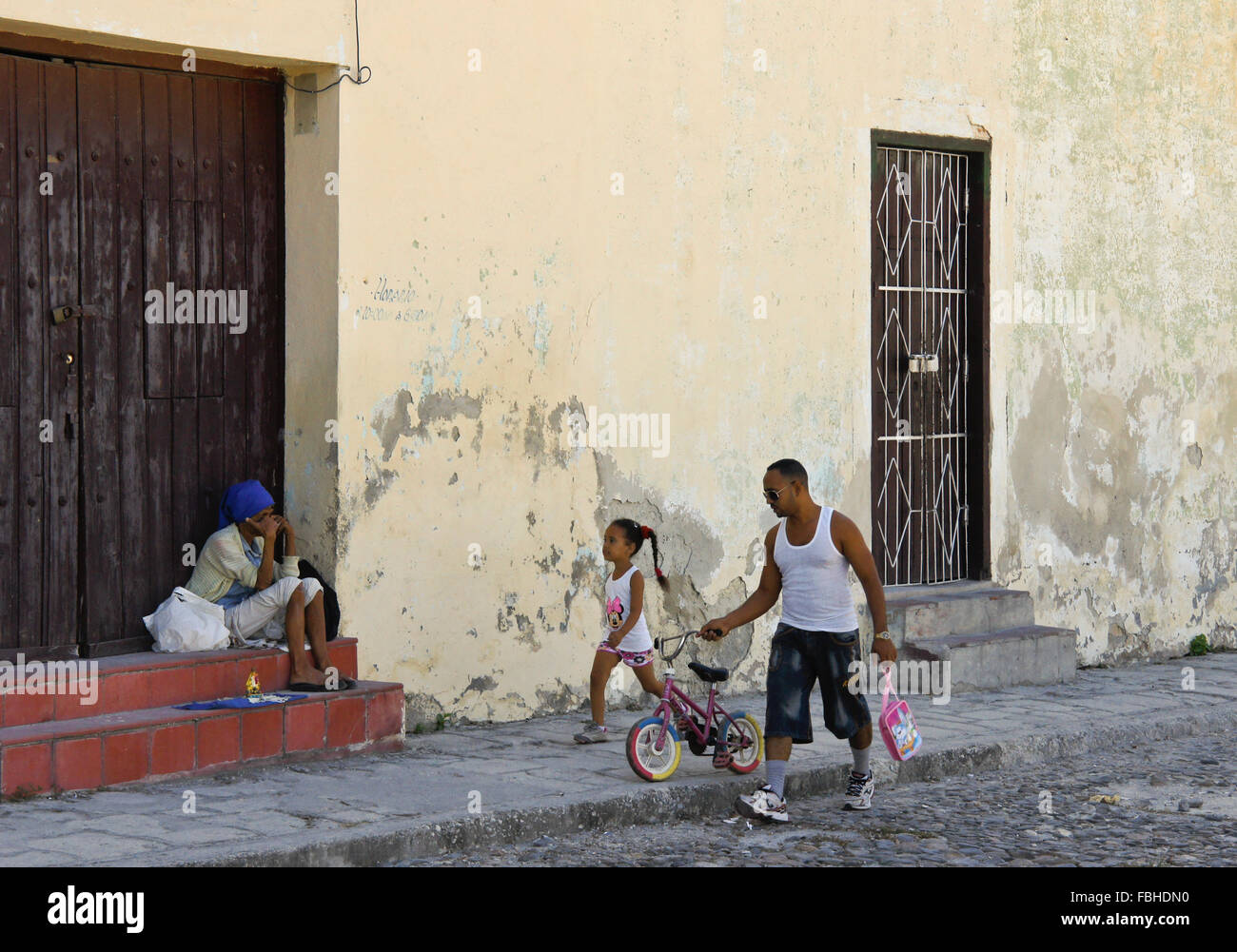 Père et fille marcher passé vieux pauvre femme mendiant dans la rue, Regla, Cuba Banque D'Images