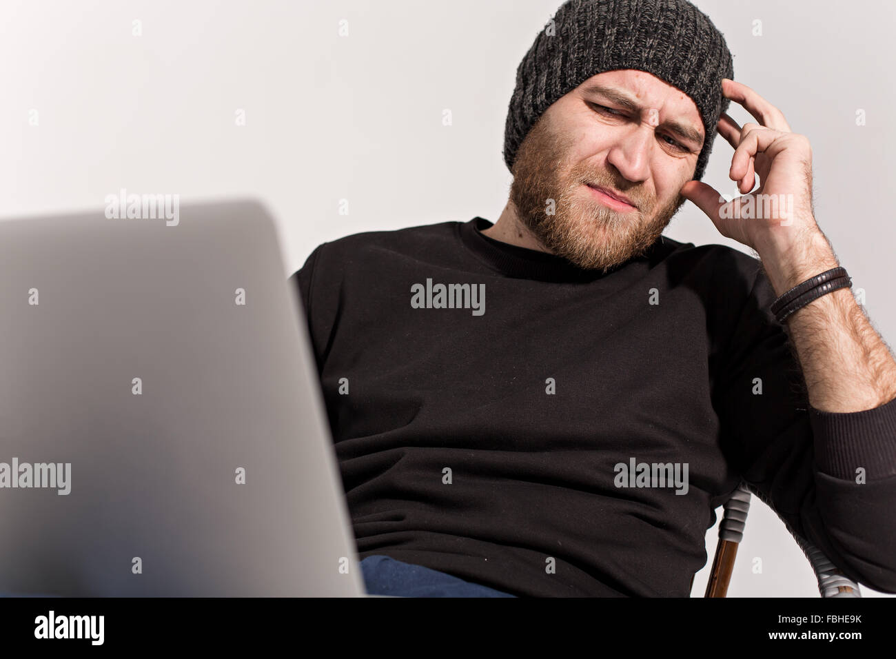 Jeune mec avec une barbe avec un ordinateur portable assis et regardant le moniteur Banque D'Images
